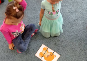 Dziewczynki układają na dywanie misie – puzzle z trzech części.